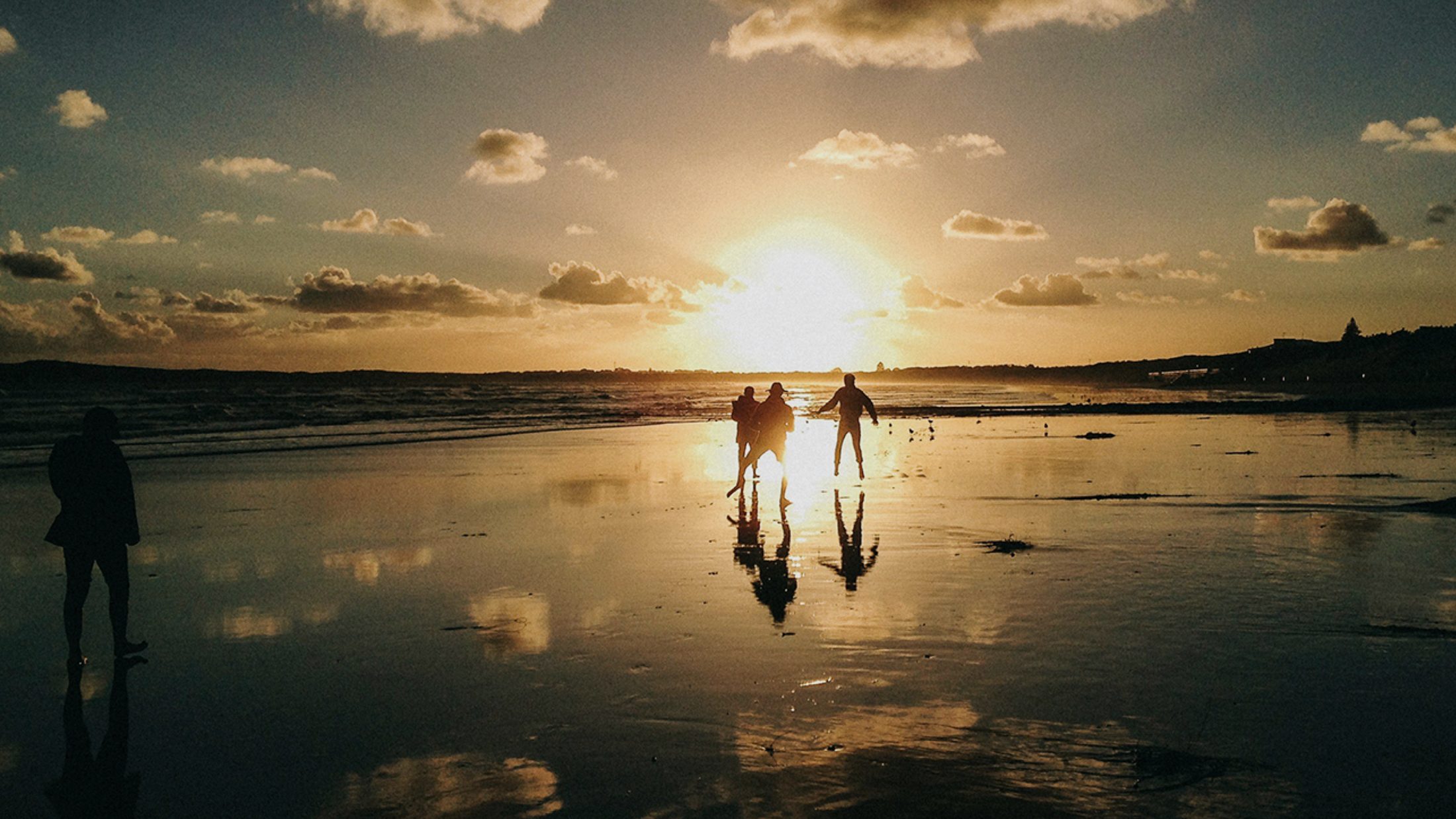 Figures walking a wide open shoreline at low sun, long reflections across wet sand